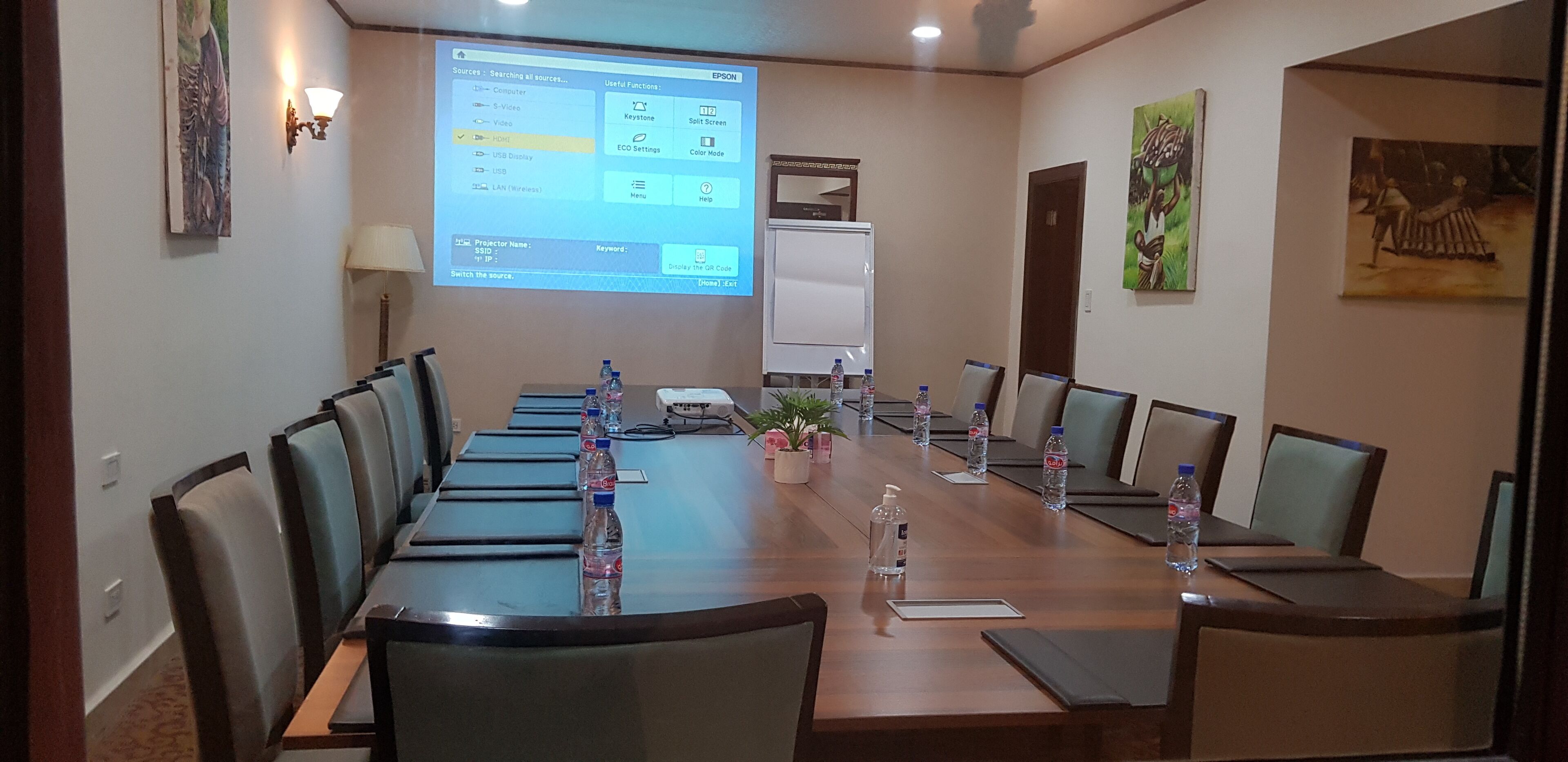 A conference room with a long table, chairs, a projector screen, and a whiteboard.