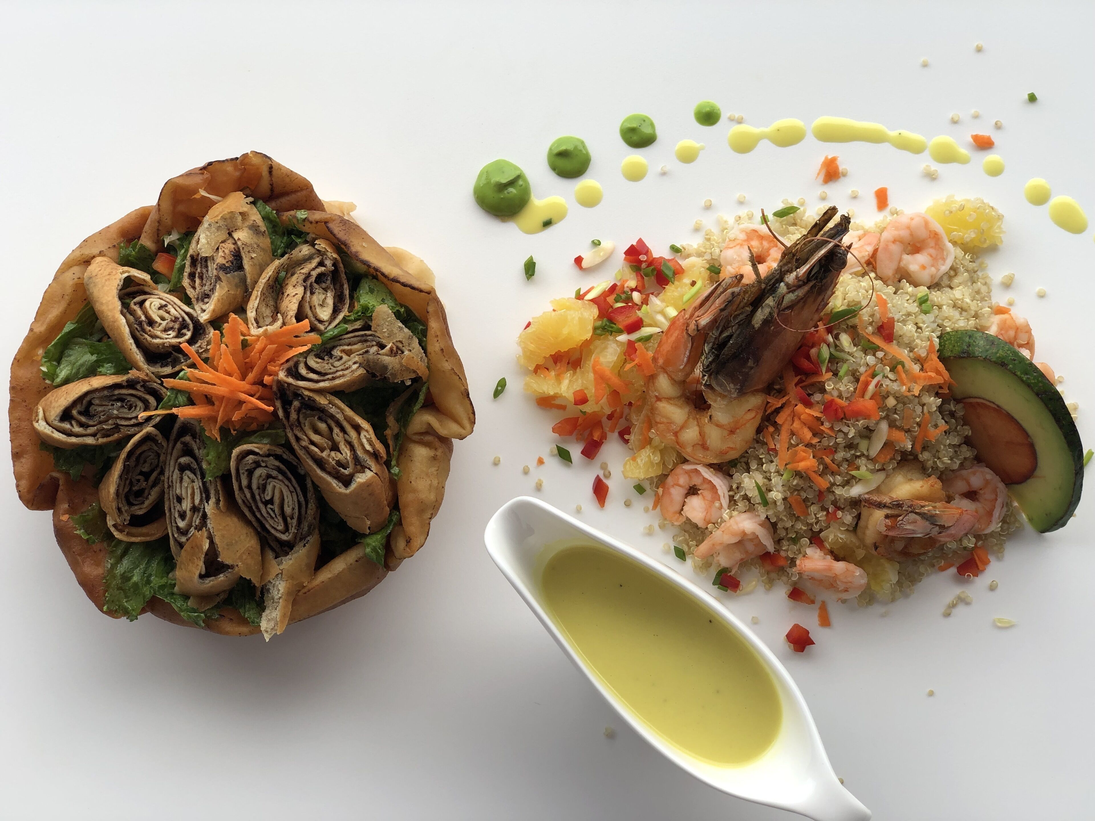 Une assiette contenant des rouleaux de viande, des légumes et des crevettes, ainsi qu’un bol de salade de quinoa avec des crevettes, de l’avocat et des légumes.