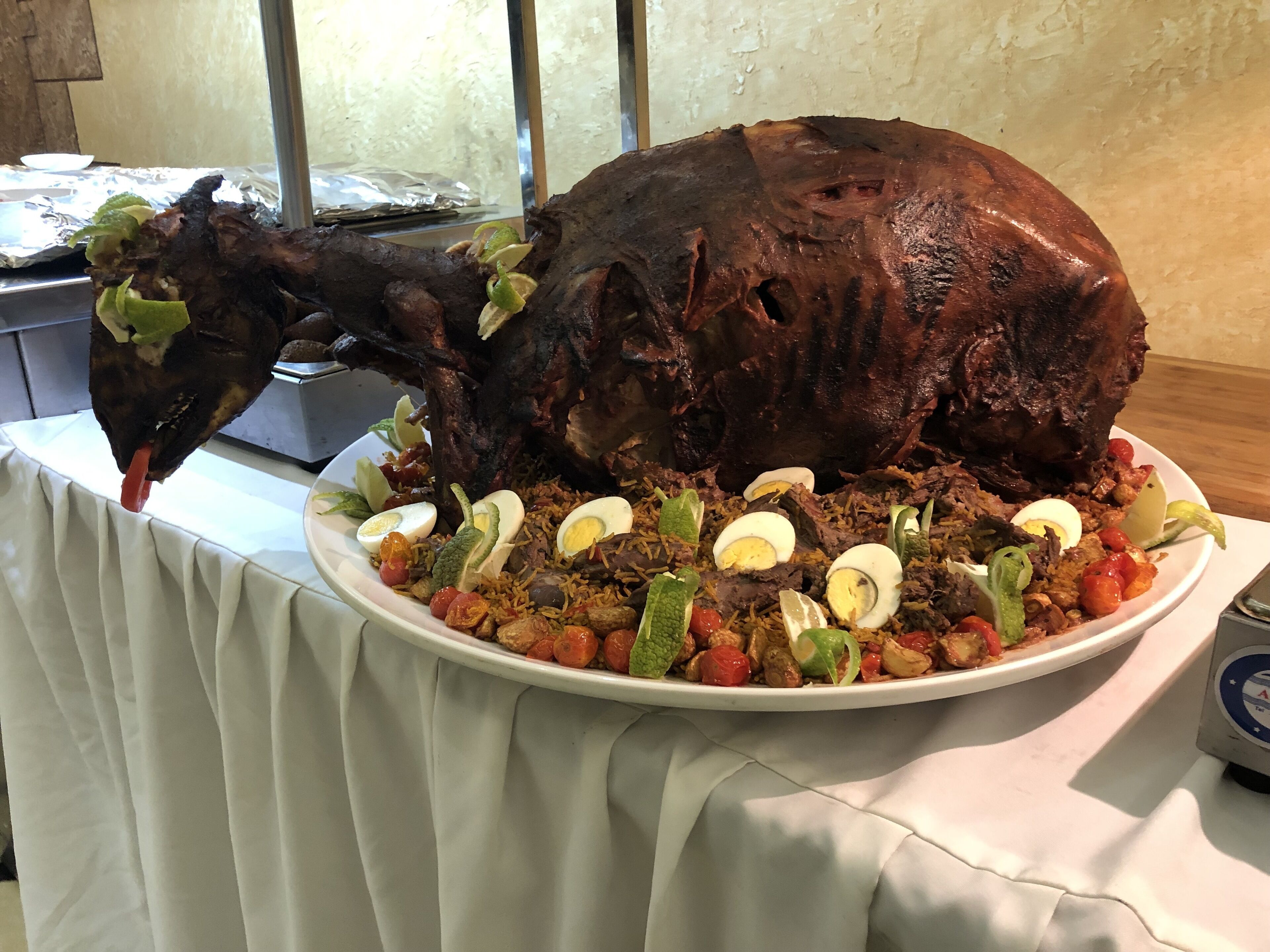 A large roasted pig on a white platter with rice, boiled eggs, and vegetables.