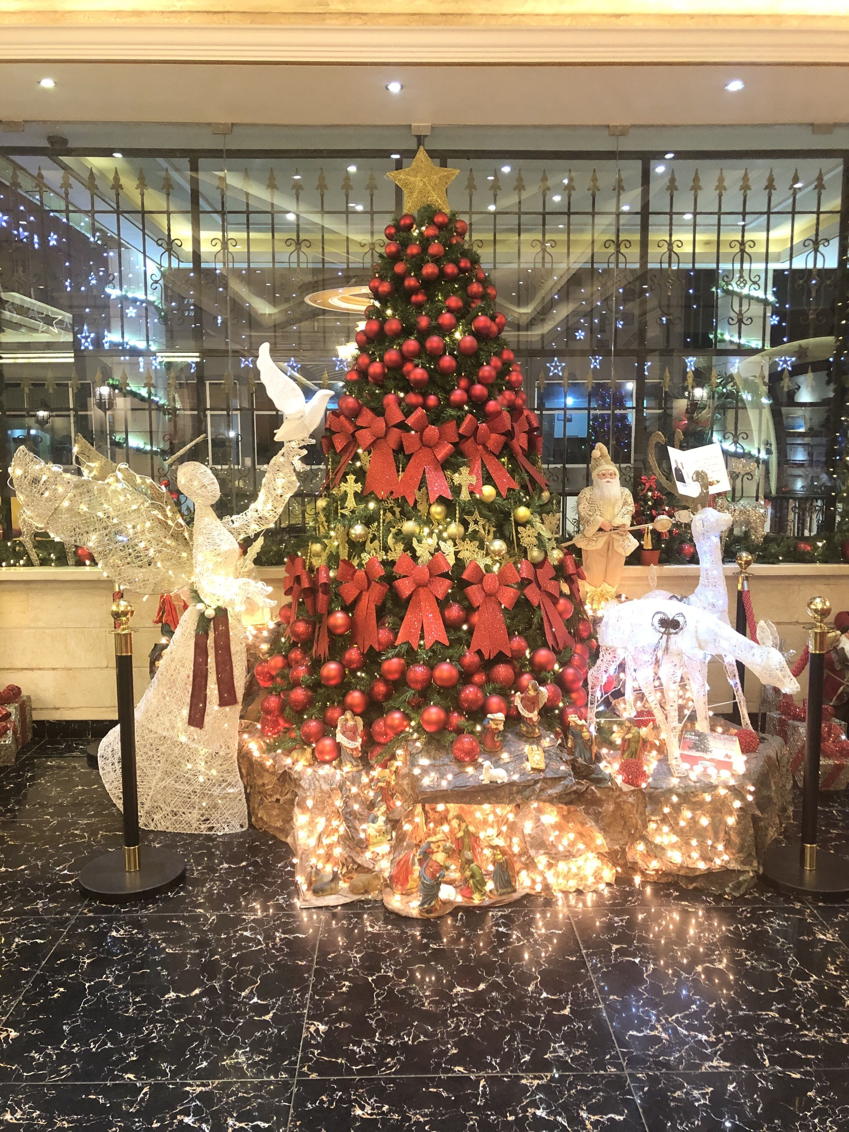 Ein Weihnachtsbaum mit roten Verzierungen und einem Stern auf der Spitze, umgeben von verschiedenen Dekorationen und Figuren.