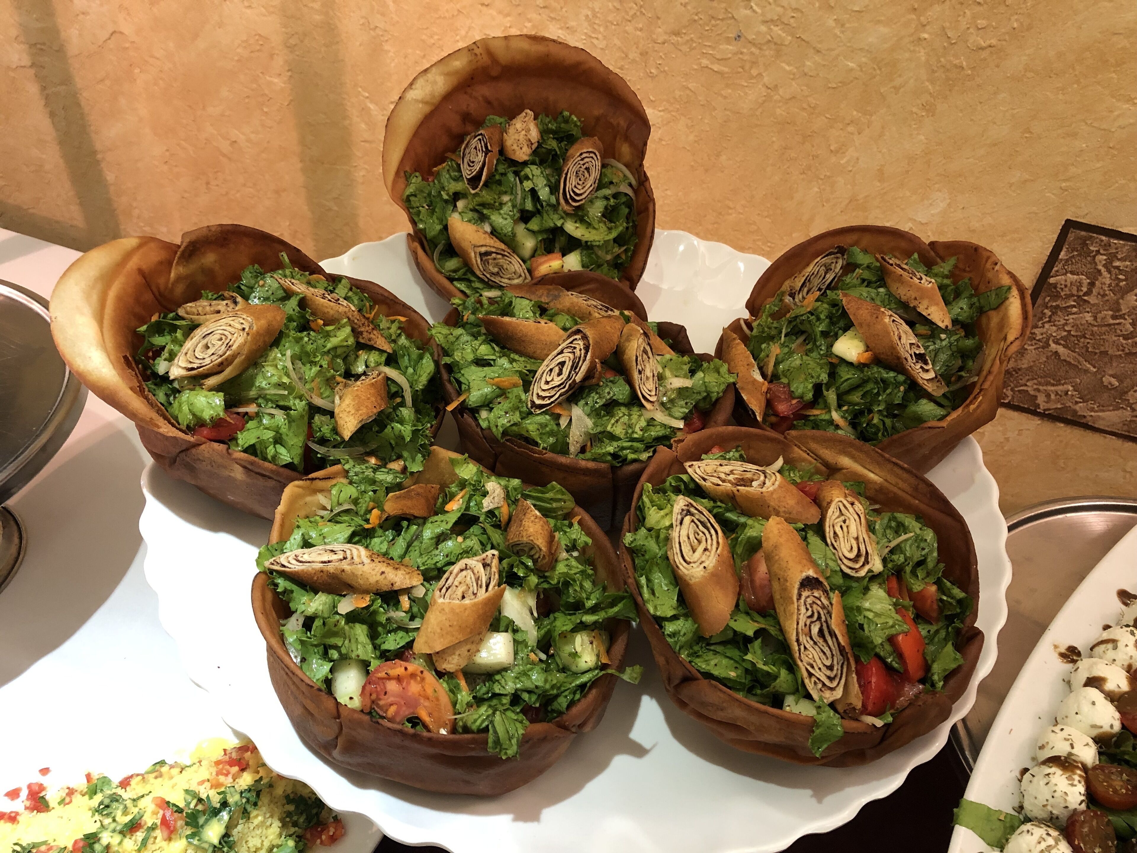 A table with five bowls of salad, each containing lettuce, tomatoes, and rolled pastry.