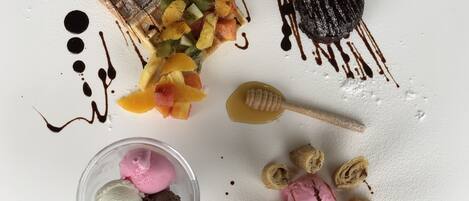 Une assiette de dessert avec une gaufre, des fruits, du chocolat et de la glace.