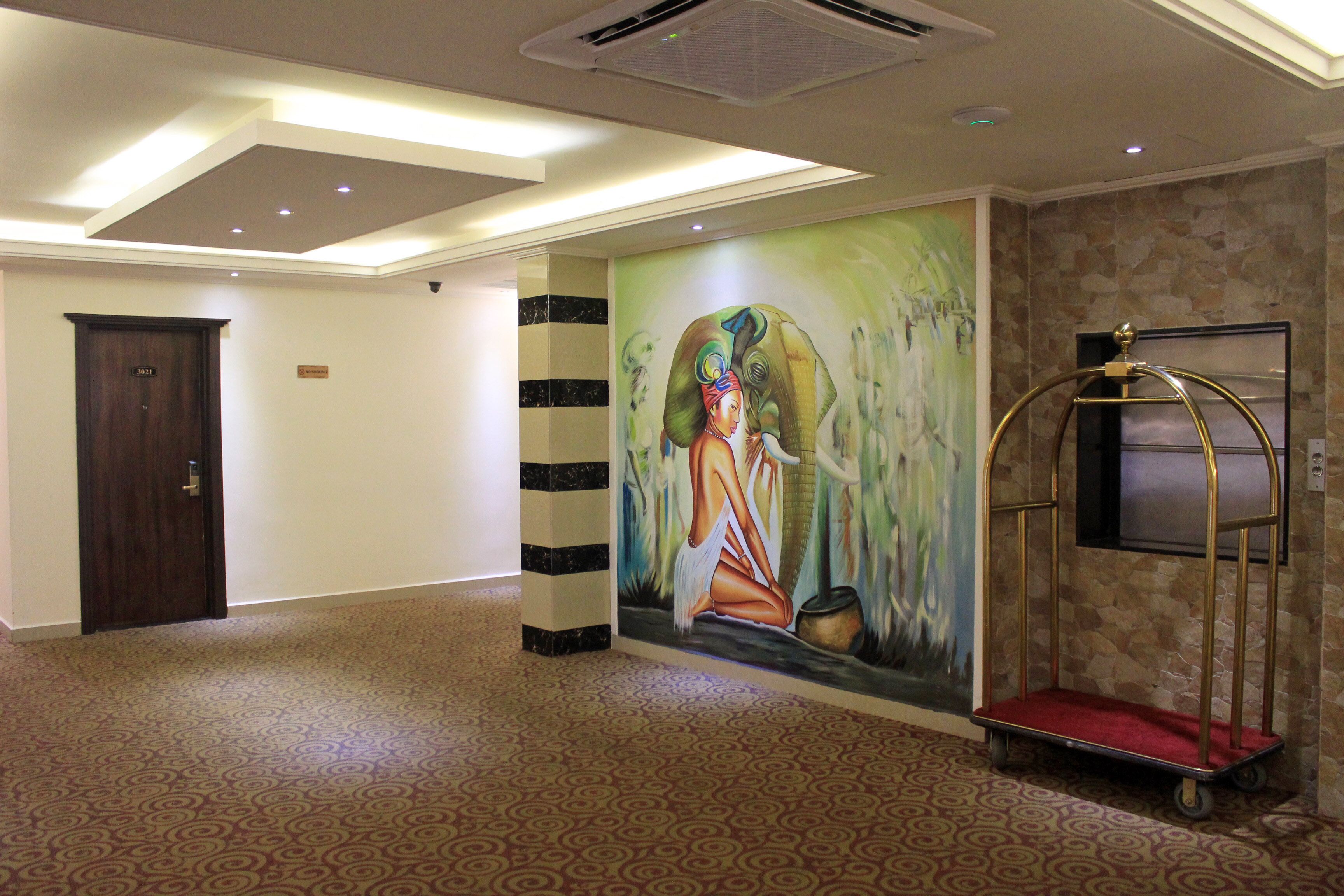 A hallway with a patterned carpet, a door, a wall mural, and a cart.