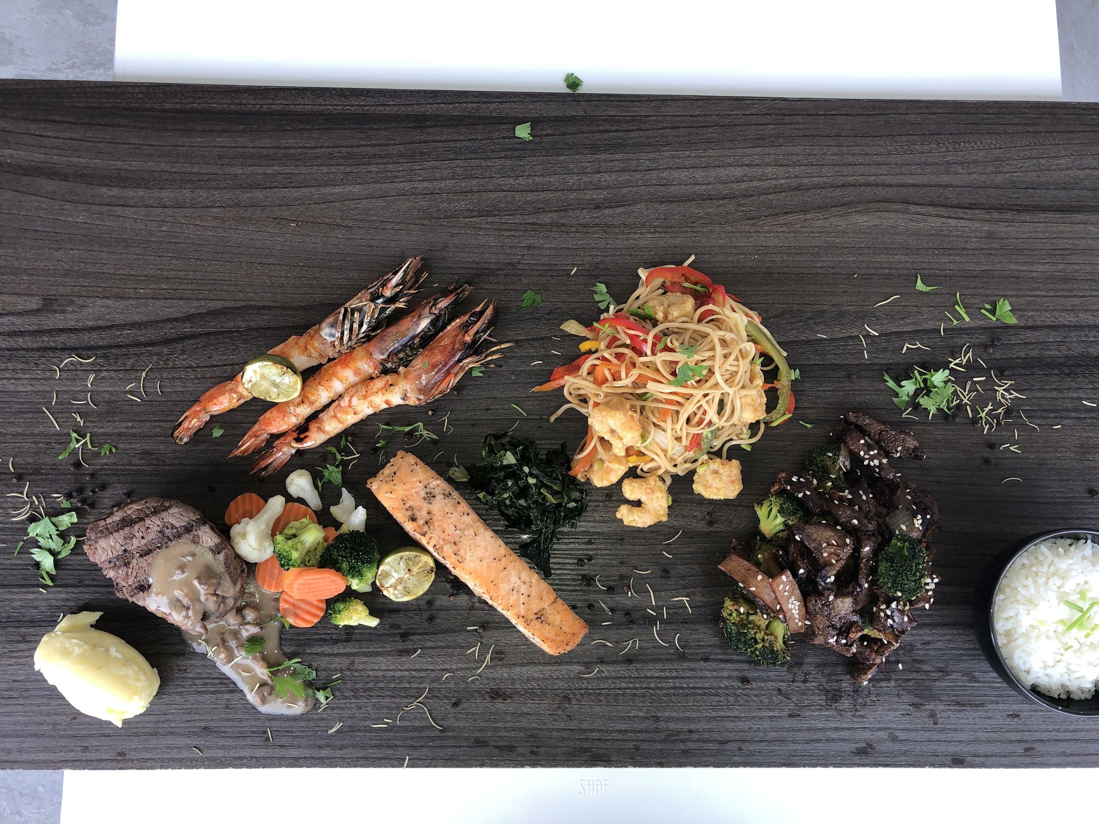 A variety of dishes including grilled meat, shrimp, and vegetables on a wooden table.