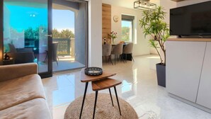 A modern living room with a sofa, a coffee table, and a TV on a cabinet. There is a dining area with chairs and a table, and a balcony with a view. - Wing 77 by Interhome (Pula)