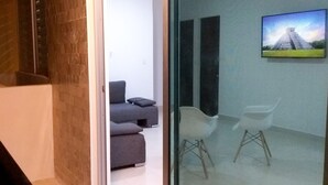 A modern living room with a glass partition, a gray sofa, and a white chair. - 58th Ave. Apartment (Playa del Carmen)