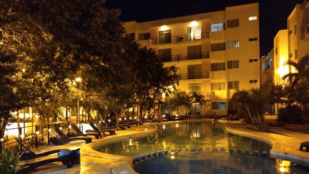 A nighttime view of a hotel pool area with lounge chairs and a building in the background. - 58th Ave. Apartment (Playa del Carmen)