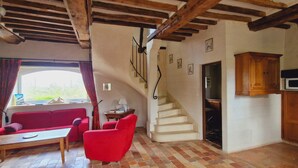 A cozy living room with a red sofa, a wooden table, a staircase leading to a kitchen area with a microwave and wooden cabinets. - Le domaine des roseraies, gîte les roseraies (Monfréville)