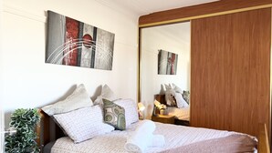 Una cama bien hecha con ropa de cama estampada, una lámpara de noche y una planta en maceta.