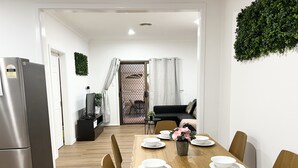 Una cocina moderna con un refrigerador de acero inoxidable, una mesa de comedor de madera con platos y tazones blancos, y una planta en maceta sobre la mesa.