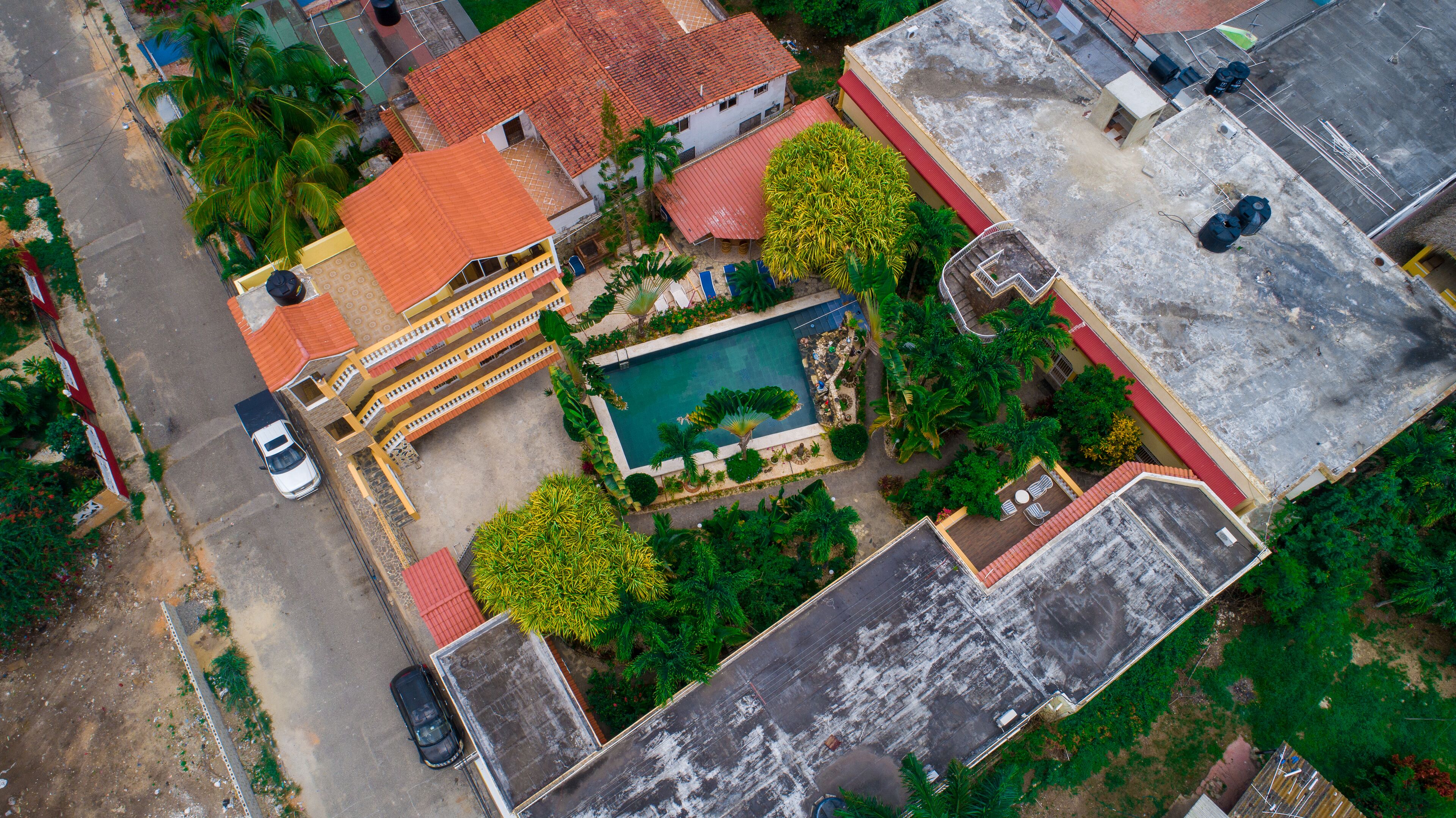 An aerial view of a residential area with a swimming pool, a red-roofed building, and a parked car.