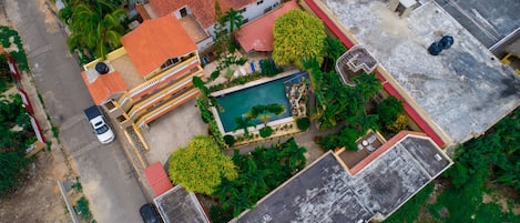 An aerial view of a residential area with a swimming pool, a red-roofed building, and a parked car.