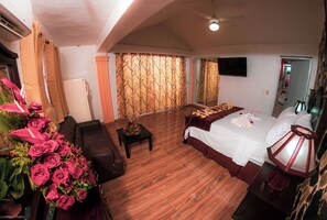 Ein Hotelzimmer mit einem Bett, einem kleinen Tisch mit Blumenvase, einer Couch und einem Fernseher an der Wand.