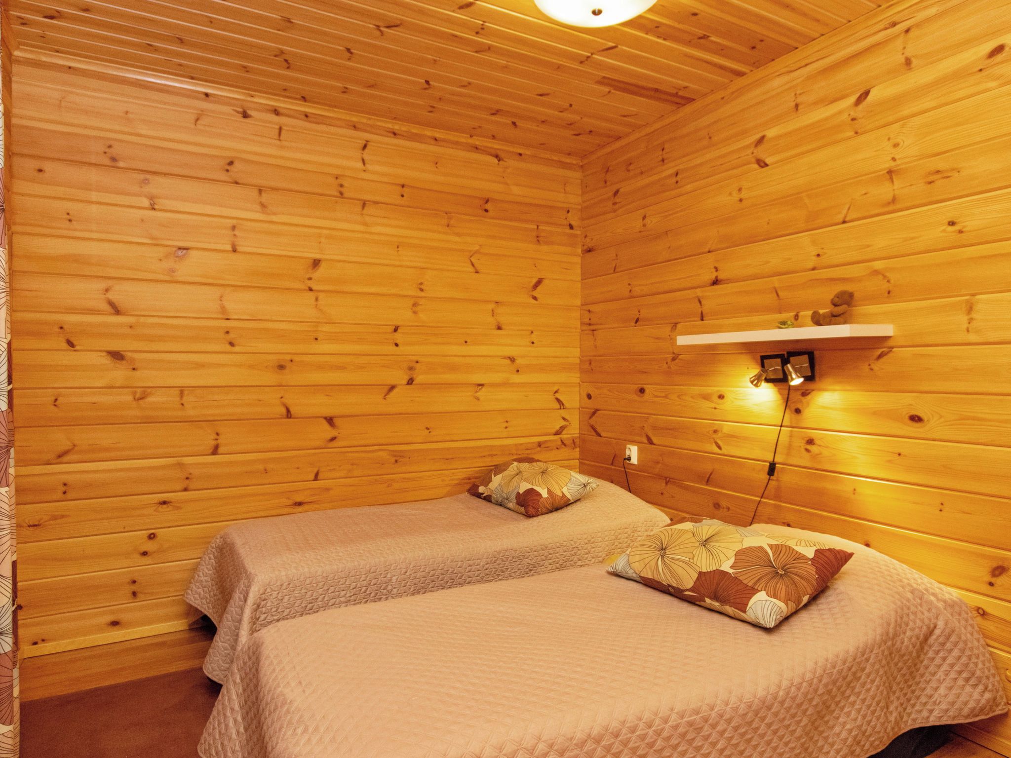 A room with wooden walls and two beds with matching quilts.