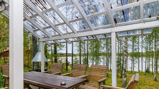 Un área de estar al aire libre techada con una mesa y sillas, con vistas a un lago.