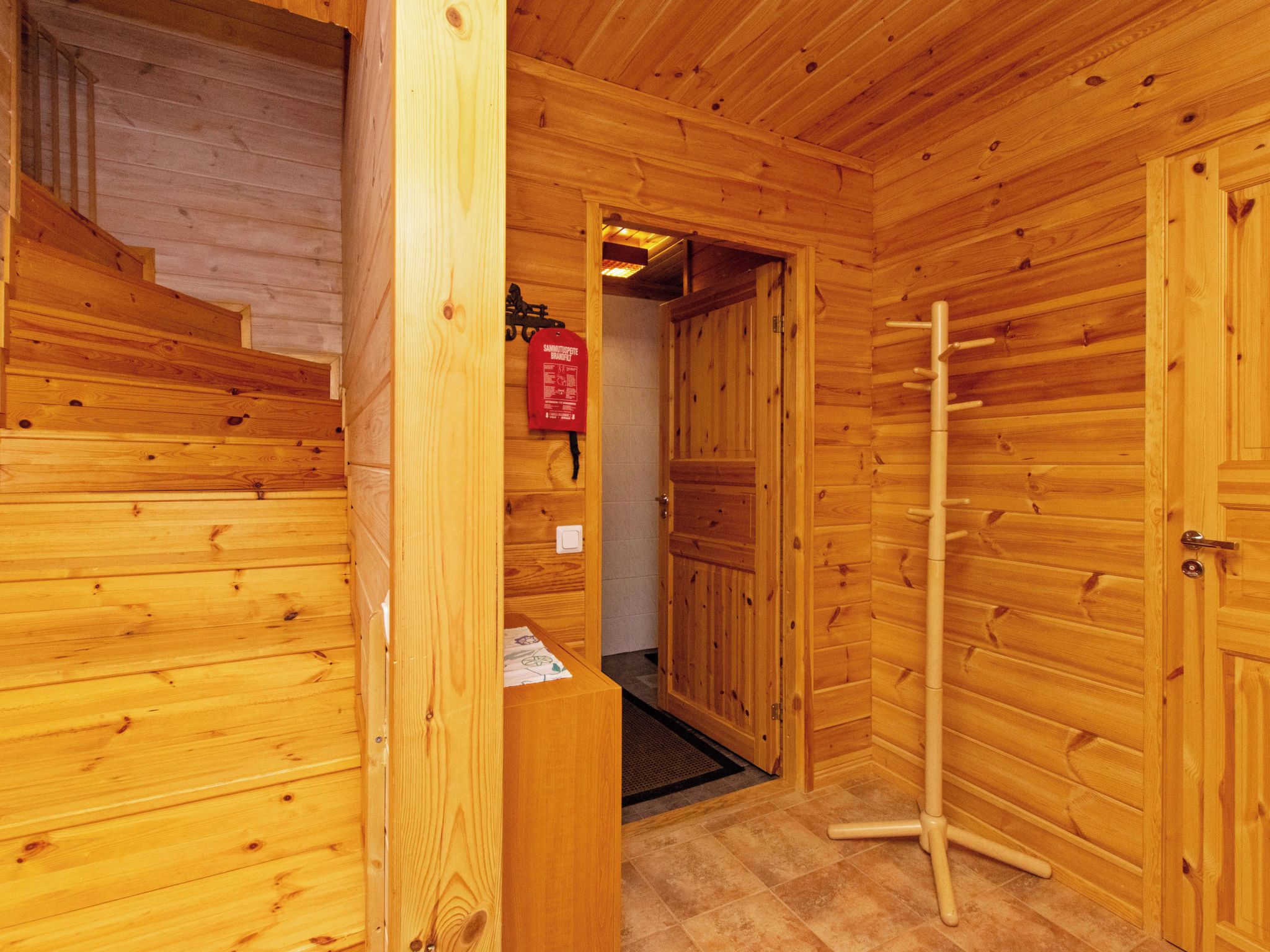 A wooden interior with a staircase, a door with a fire extinguisher, and a towel rack.