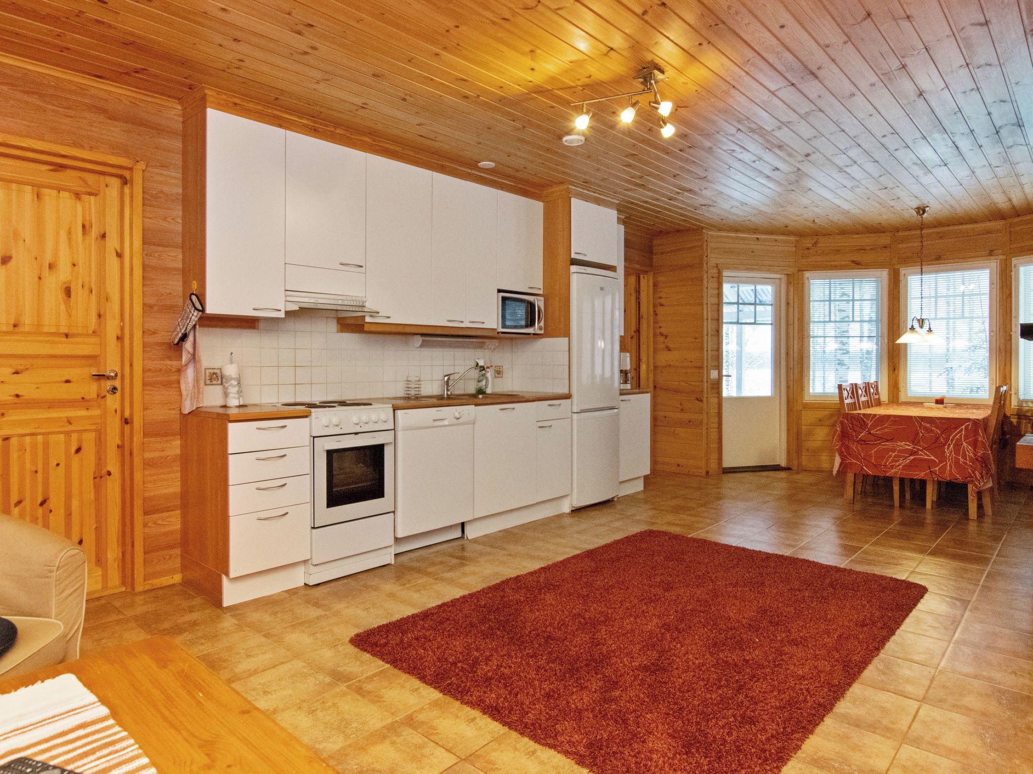A wooden interior with a kitchen, dining area, and a red rug.
