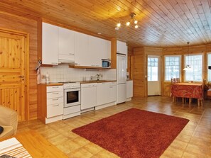 A wooden interior with a kitchen, dining area, and a red rug.