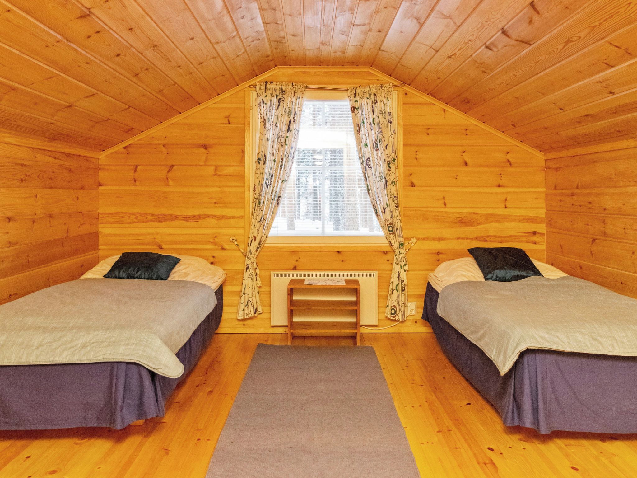A cozy attic bedroom with two beds, a window with patterned curtains, and a small table.