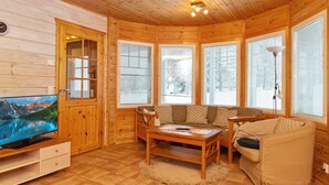 Interior acogedor de una cabaña con paredes de madera, un televisor, un sofá, una mesa de centro y ventanas amplias.