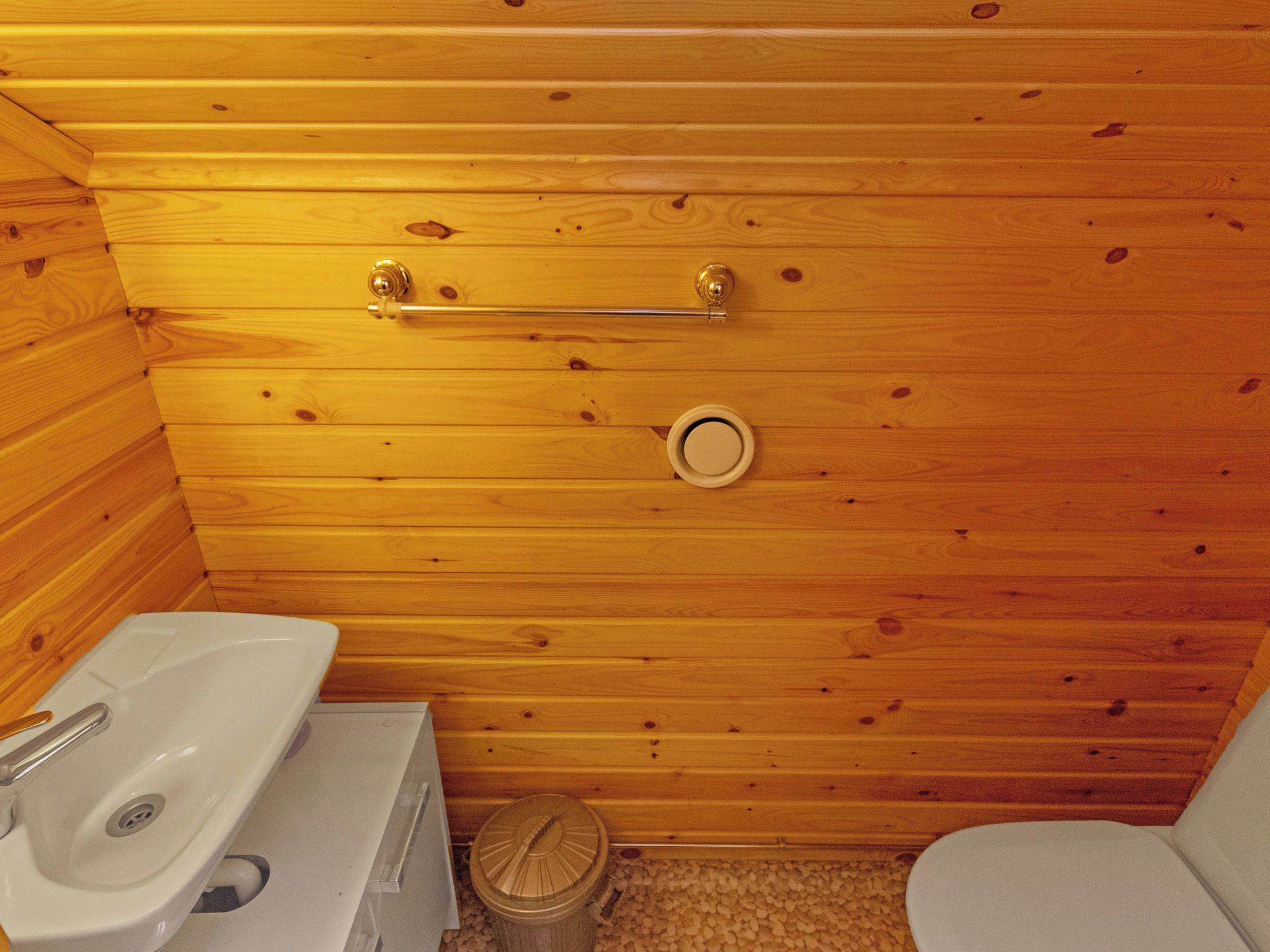 A small, wooden-paneled bathroom with a toilet, sink, and a trash bin.