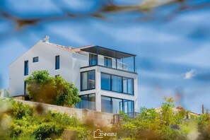 Stunning two-story residence with a flat roof and balcony, surrounded by lush greenery and large windows.
