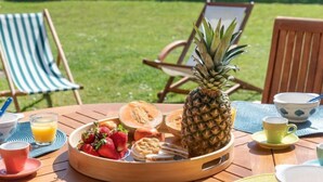 Uma mesa de madeira com um prato de frutas, uma abacaxi e um copo de suco de laranja.