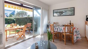 Uma sala de jantar com uma mesa posta para quatro pessoas, uma janela grande com vista para um jardim e edifícios, e um quadro na parede.