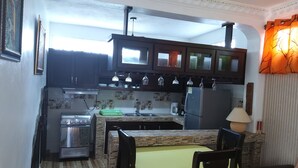A compact kitchen with dark cabinets, a gas stove, a refrigerator, and a dining area with a table and chairs. - Deluxe Apartment (14) RESIDENCE TROPICAL GARDEN (Boca Chica)