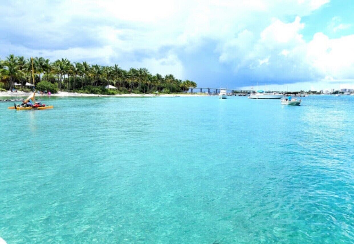 A coastal scene with clear turquoise water, a small boat, and a distant bridge.