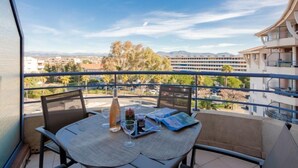 A balcony with a table set for two, a bottle, and glasses, overlooking a cityscape with buildings and palm trees. - Résidence Aigue Marine by Interhome (Fréjus)