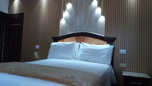 Una cama bien hecha con sábanas blancas y un cabecero de madera, frente a una pared con paneles de madera verticales e iluminación empotrada.
