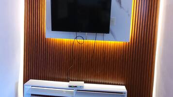 Una sala de estar moderna con un televisor de pantalla plana montado en una pared de paneles de madera, un mueble blanco de entretenimiento debajo y piso de madera con diseño.