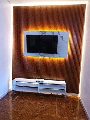 Una sala de estar moderna con un televisor de pantalla plana montado en una pared de paneles de madera, un mueble blanco de entretenimiento debajo y piso de madera con diseño.