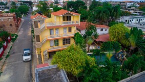 Un immeuble jaune à plusieurs étages, doté de balcons, entouré d’une végétation luxuriante et d’autres immeubles d’habitation.