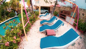 A poolside area with lounge chairs, a barbecue, and a stone wall. - Deluxe Apartment (7) RESIDENCE TROPICAL GARDEN (Boca Chica)
