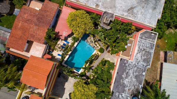 Vista aérea de una zona residencial con una piscina rodeada de vegetación y edificios de techo rojo.