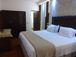 Habitación de hotel con una cama grande, un armario y un baño visible a través de una puerta abierta.