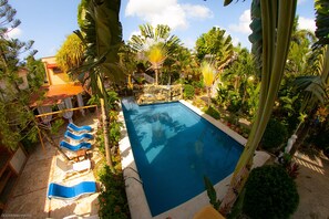 Una piscina rodeada de plantas tropicales y un edificio con techo rojo.