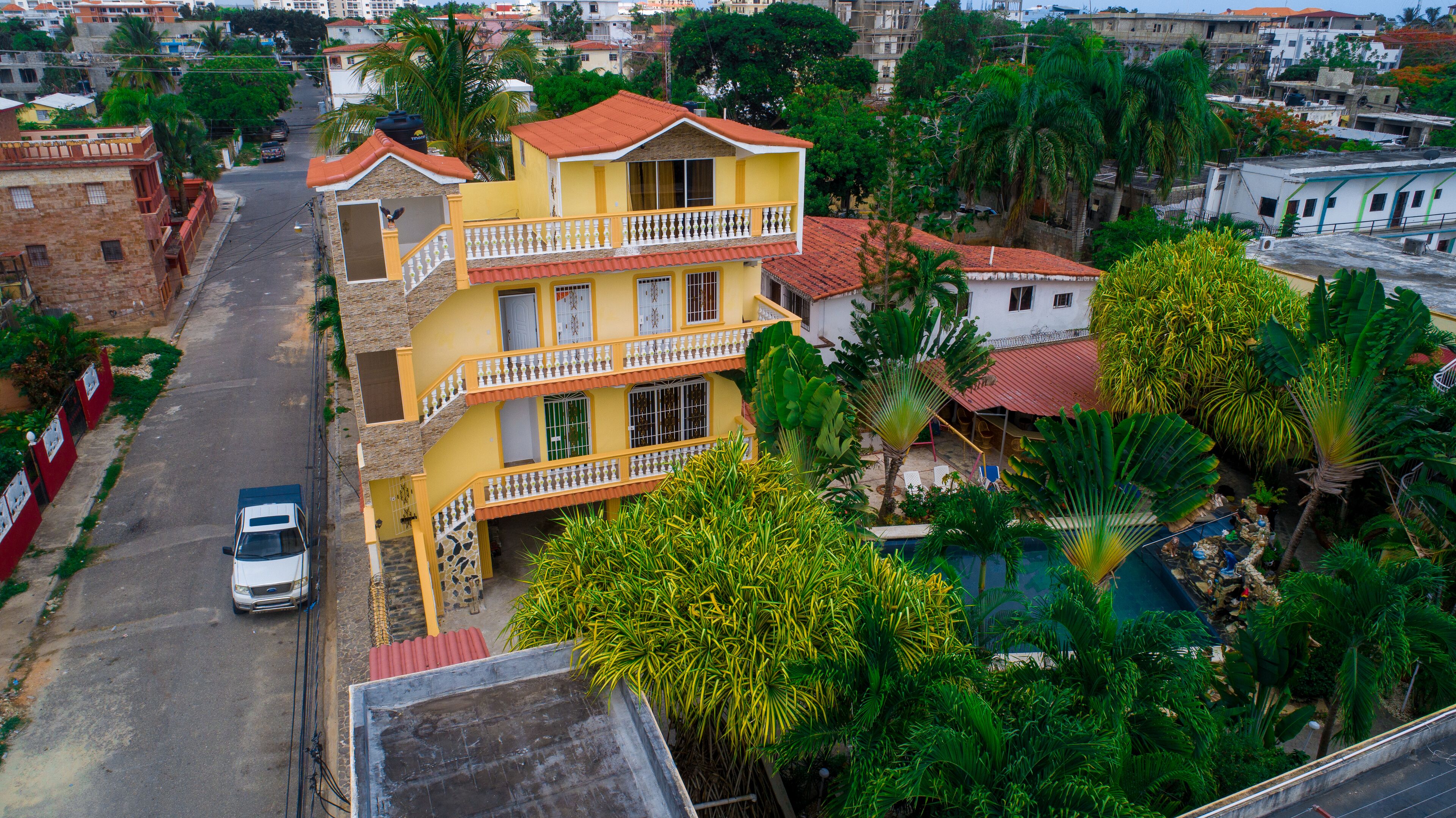 Un immeuble jaune à plusieurs étages, doté de balcons, entouré d’une végétation luxuriante et d’autres immeubles d’habitation.