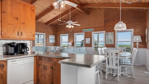 A spacious kitchen with wooden cabinets, a dishwasher, and a dining area with a table and chairs. - SEMI OCEANFRONT, Steps to the Beach, Unobstructed Amazing Ocean Views. Remodeled (Kitty Hawk)