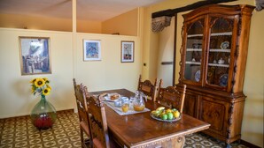 A dining room with a wooden table set for breakfast, surrounded by chairs, a cabinet with glass doors, and patterned floor tiles.