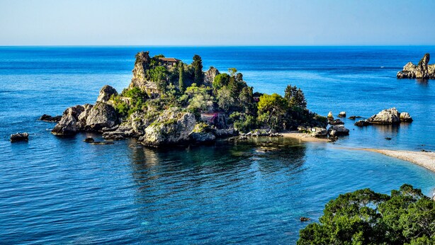 A coastal island with rocky terrain and sparse vegetation, surrounded by calm blue waters.