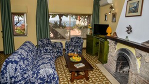 A living room with a sofa set, a coffee table with fruit, a fireplace, and a view through a window.