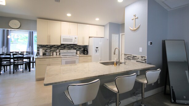 A modern kitchen with white cabinets, a large island with bar stools, a microwave, and a refrigerator. - Newly Renovated, Beautiful Spacious House With Heated Pool. (Englewood)