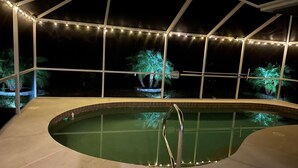 An indoor swimming pool with a view of palm trees outside, surrounded by a glass enclosure with string lights. - Newly Renovated, Beautiful Spacious House With Heated Pool. (Englewood)