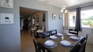 A dining area with a wooden table set for six, surrounded by chairs. There are framed pictures on the walls, a chandelier hanging above, and a window with curtains. - Newly Renovated, Beautiful Spacious House With Heated Pool. (Englewood)