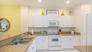 A kitchen with white cabinets, a granite countertop, a stainless steel sink, a microwave, and an oven.