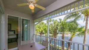 A balcony with a table and chairs, overlooking a body of water and palm trees.
