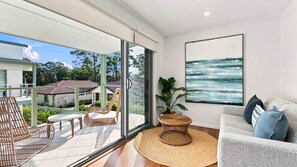 A modern interior with a glass door leading to an outdoor area, a wicker chair, a round woven table, and a sofa with cushions.